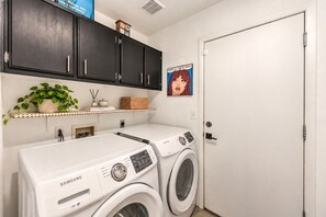 A laundry room with a Samsung washer and dryer, a shelf with a plant and decorative items, and a door with a cartoon character. - Vegas Designer Private Pool Oasis, King Suite, BBQ (Las Vegas)