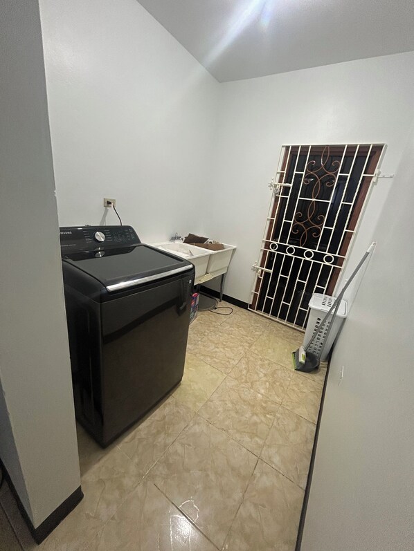 A compact laundry room with a washing machine, a drying rack, and a small sink.