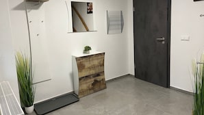 A modern interior with a white wall, a wooden cabinet with a plant, a door, and a vent. - Anton Günther by Interhome (Bernsbach)