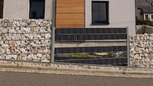 A modern two-story house with a stone foundation, a wooden accent wall, and a metal fence. - Anton Günther by Interhome (Bernsbach)