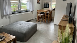 A modern living room with a grey sofa, a wooden dining table with chairs, a kitchen area with a stove and microwave, and a TV on a wooden stand. - Anton Günther by Interhome (Bernsbach)