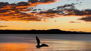 Um pôr do sol sobre águas calmas, com silhuetas de montanhas ao fundo.