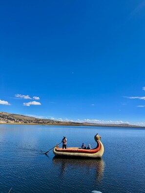 A traditional boat with a figurehead on a calm lake, surrounded by a clear blue sky and distant hills.
