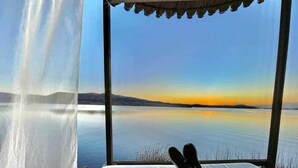 Cama com vista para um lago tranquilo e montanhas ao pôr do sol.