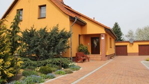 Ein gelbes Gebäude mit einer Ziegel-Einfahrt, einer hölzernen Bank und einem Garten mit verschiedenen Pflanzen und Blumen.