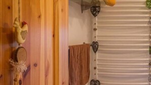Eine Holztür mit einem Metallbeschlag, ein kleiner Holzschemel und Dekorationsobjekte, darunter eine Hühnerfigur und herzförmige Verzierungen.