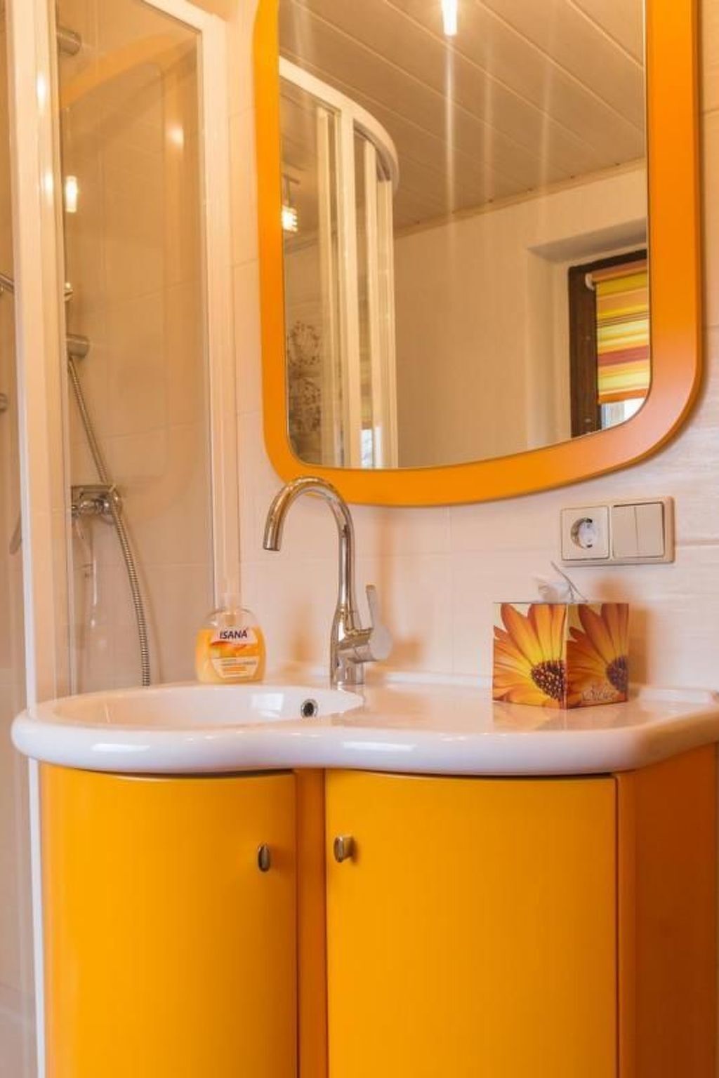 A bathroom with a white sink, yellow cabinets, a mirror, and a shower.