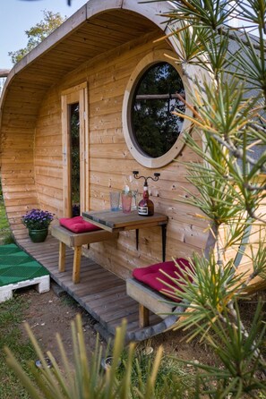 A wooden pod-style cabin with a circular window, a small table with red cushions, and a potted plant. - mit Fasssauna by Interhome (Bautzen)