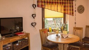 A cozy dining area with a round wooden table, four chairs, a television on a wooden stand, and a window with blinds. - Wohnung in Niedergurig mit Grill, Sauna und Gart by Interhome (Bautzen)