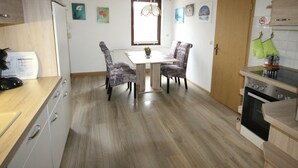 Een keuken met een eettafel en stoelen, houten kastjes, een fornuis en een raam met gordijnen.