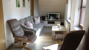 Een moderne woonkamer met een bank, twee fauteuils, een televisie en een bijzettafeltje.