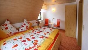 Een slaapkamer met een houten plafond, een bed met een bloemenprint, twee rode stoelen en een kleine tafel.
