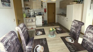 Een eethoek met een tafel gedekt voor vier personen, omringd door gestreept beklede stoelen. Boven de tafel hangt een kroonluchter, en op de achtergrond staan houten kastjes en een magnetron.