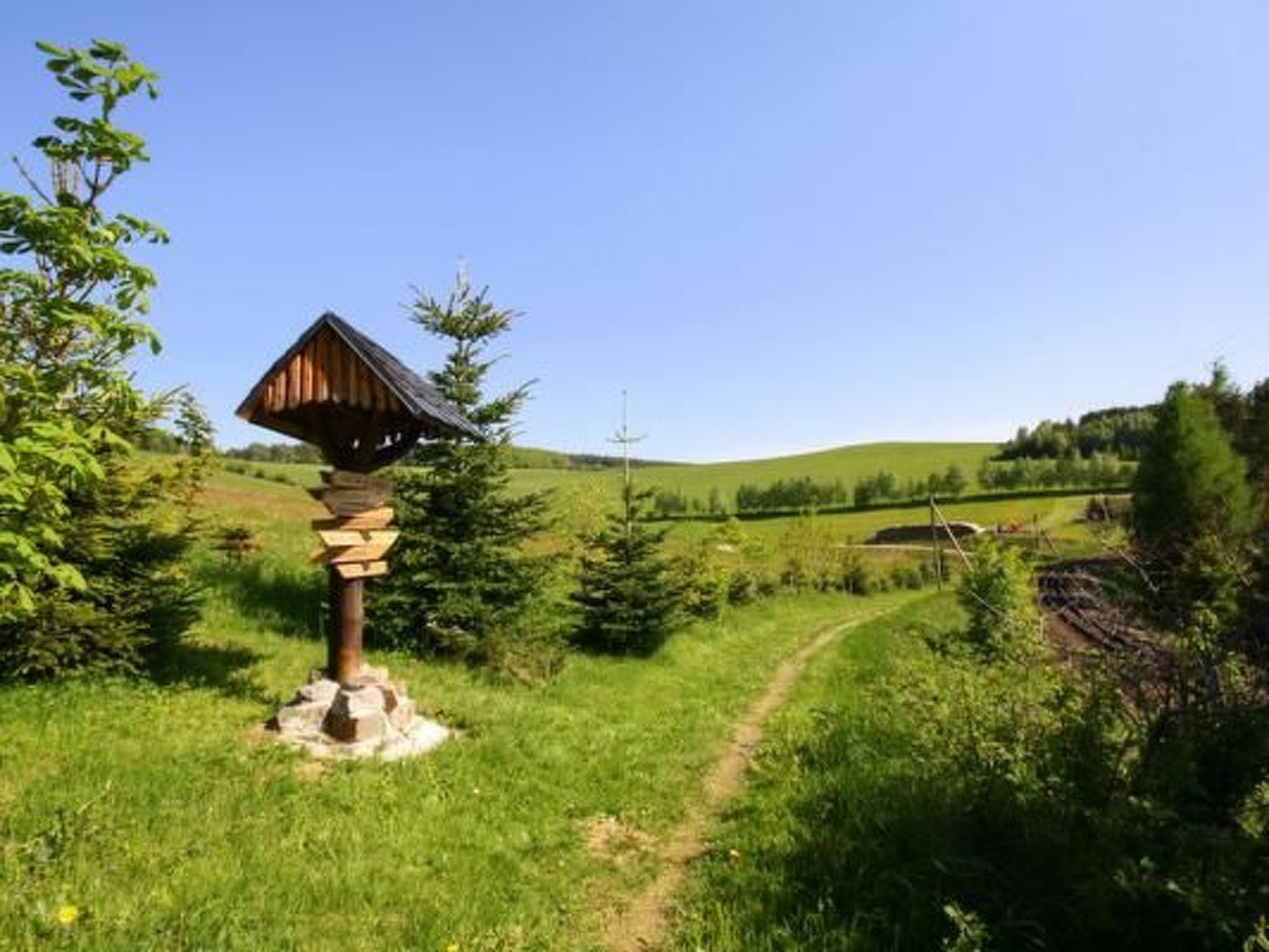 Eine Holzhütte mit geneigtem Dach, möglicherweise ein Kiosk, auf einem grasbewachsenen Hügel unter blauem Himmel.