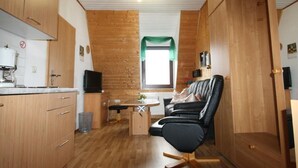 Un espacio habitable compacto con paredes y pisos de madera, una kitchenette, un comedor y una zona de estar con una silla negra.