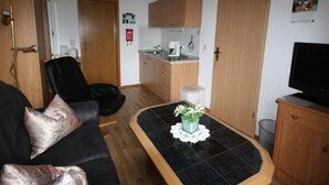 Un espacio habitable compacto con kitchenette, un sofá, un televisor y una pequeña mesa con una planta.