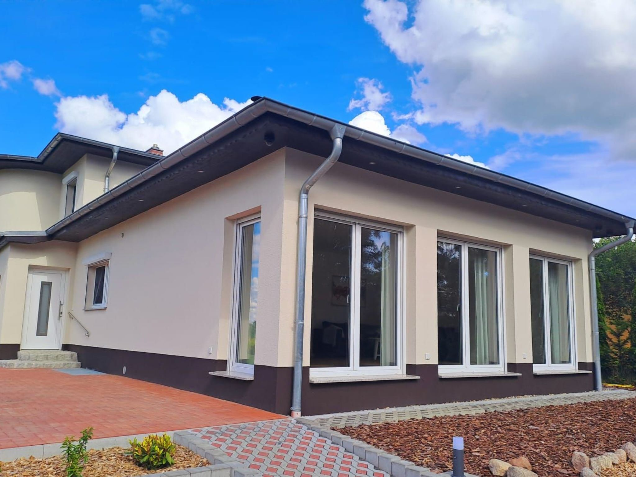 Una casa moderna de dos pisos con amplios ventanales, un camino de ladrillo y un jardín ajardinado.