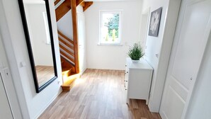 A hallway with wooden flooring, a staircase, a small window with a view of greenery, and a white cabinet with a plant. - Ferienhaus by Interhome (Frankfurt / Oder)