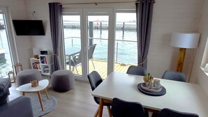 A modern living room with a white table, grey sofa, and a balcony with a view of the water. - Hausboot Tosca by Interhome (Stralsund)