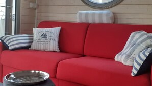 A red sofa with striped pillows, a metal bowl, and a round mirror on a wooden wall. - Hausboot NautikHus by Interhome (Werder (Havel))