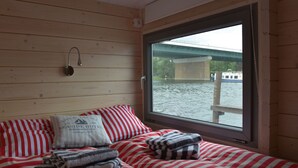 A cabin with a bed, pillows, and a window with a view of a bridge over water. - Hausboot NautikHus by Interhome (Werder (Havel))