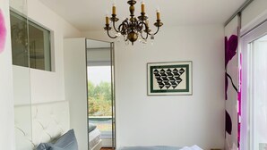 Een slaapkamer met twee bedden, een kroonluchter, een geometrisch kunstwerk in een lijst en uitzicht op een tuin door een schuifdeur.