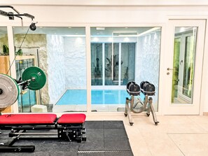 A gym with weightlifting equipment, a bench, and a pool area visible through glass doors. - UG Neubau City by Interhome (Munich)