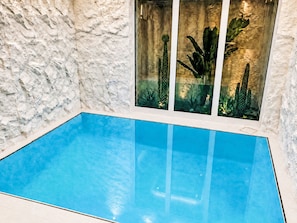 An indoor swimming pool with a textured wall and a window displaying cacti. - UG Neubau City by Interhome (Munich)