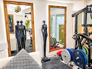 Une salle de sport équipée de matériel d’exercice, d’un miroir et de deux statues.
