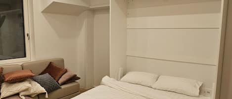 A bedroom with a large bed, a sofa, and a window.