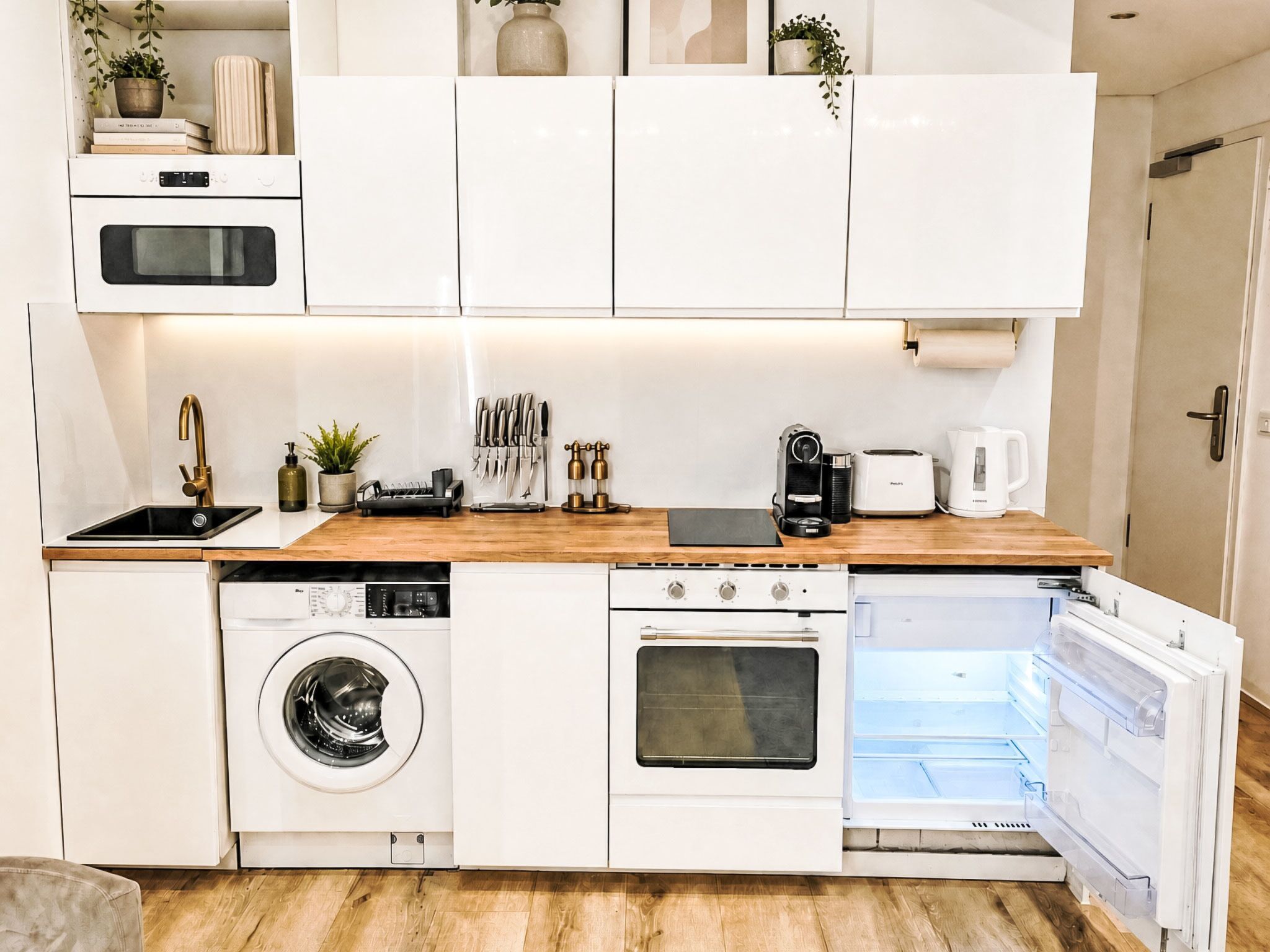 Eine kompakte Küche mit Einbaugeräten, darunter Waschmaschine, Backofen und Kühlschrank.