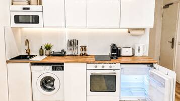 Eine kompakte Küche mit Einbaugeräten, darunter Waschmaschine, Backofen und Kühlschrank.
