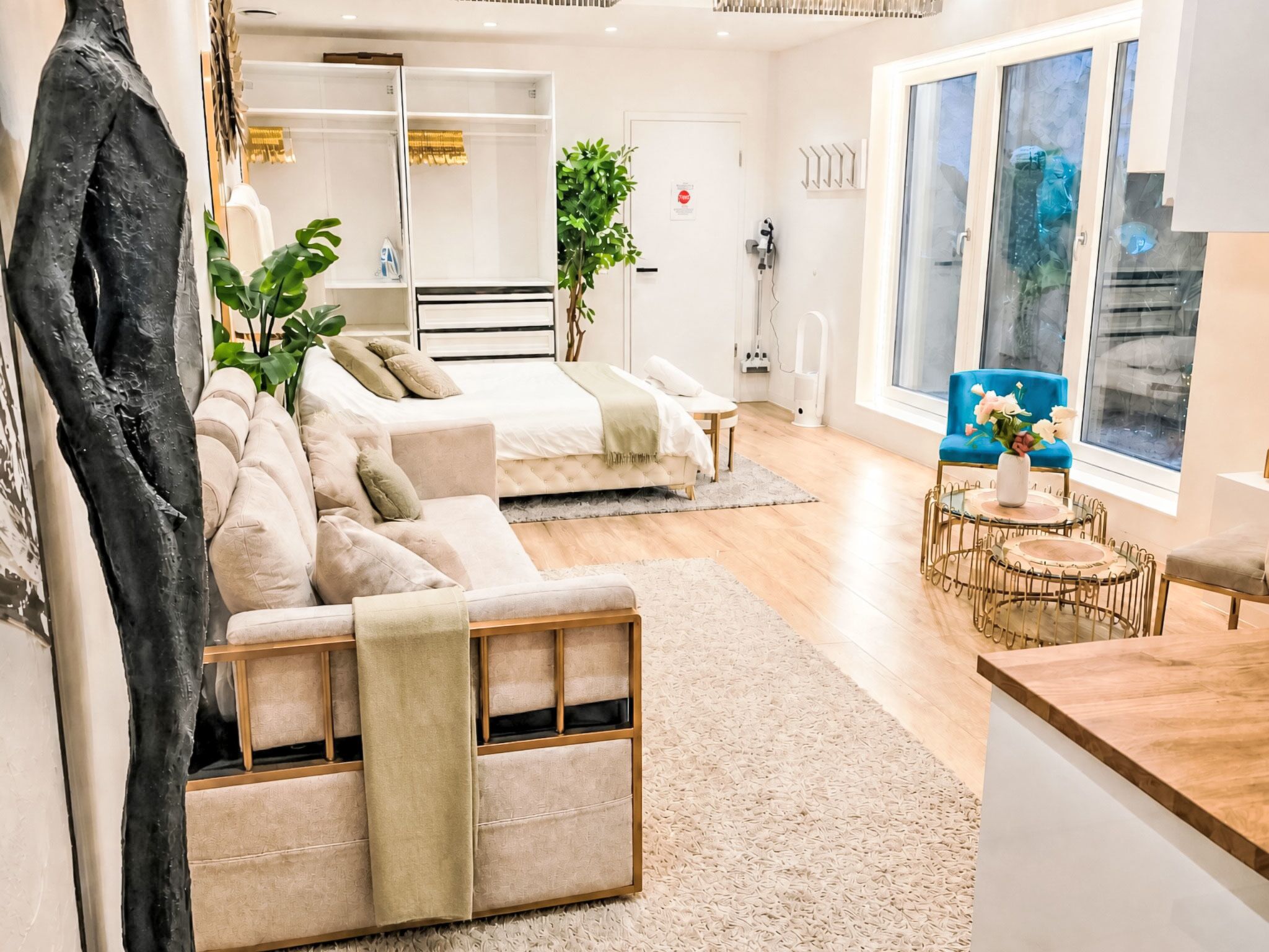 A modern living room with a sofa, a coffee table, and a blue chair. There is a large window with a view of the outdoors.