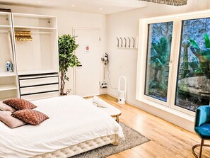Een slaapkamer met een bed, een plant, een raam met uitzicht en een stoel.