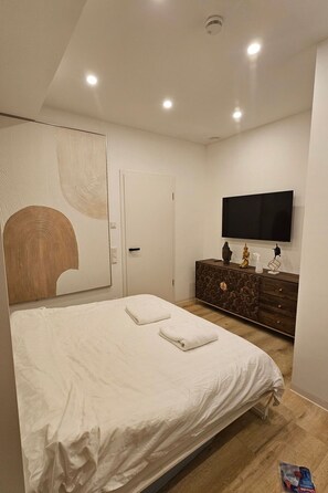 Een moderne slaapkamer met een groot bed, een dressoir, een flatscreen-tv en een opvallend kunstwerk aan de muur.