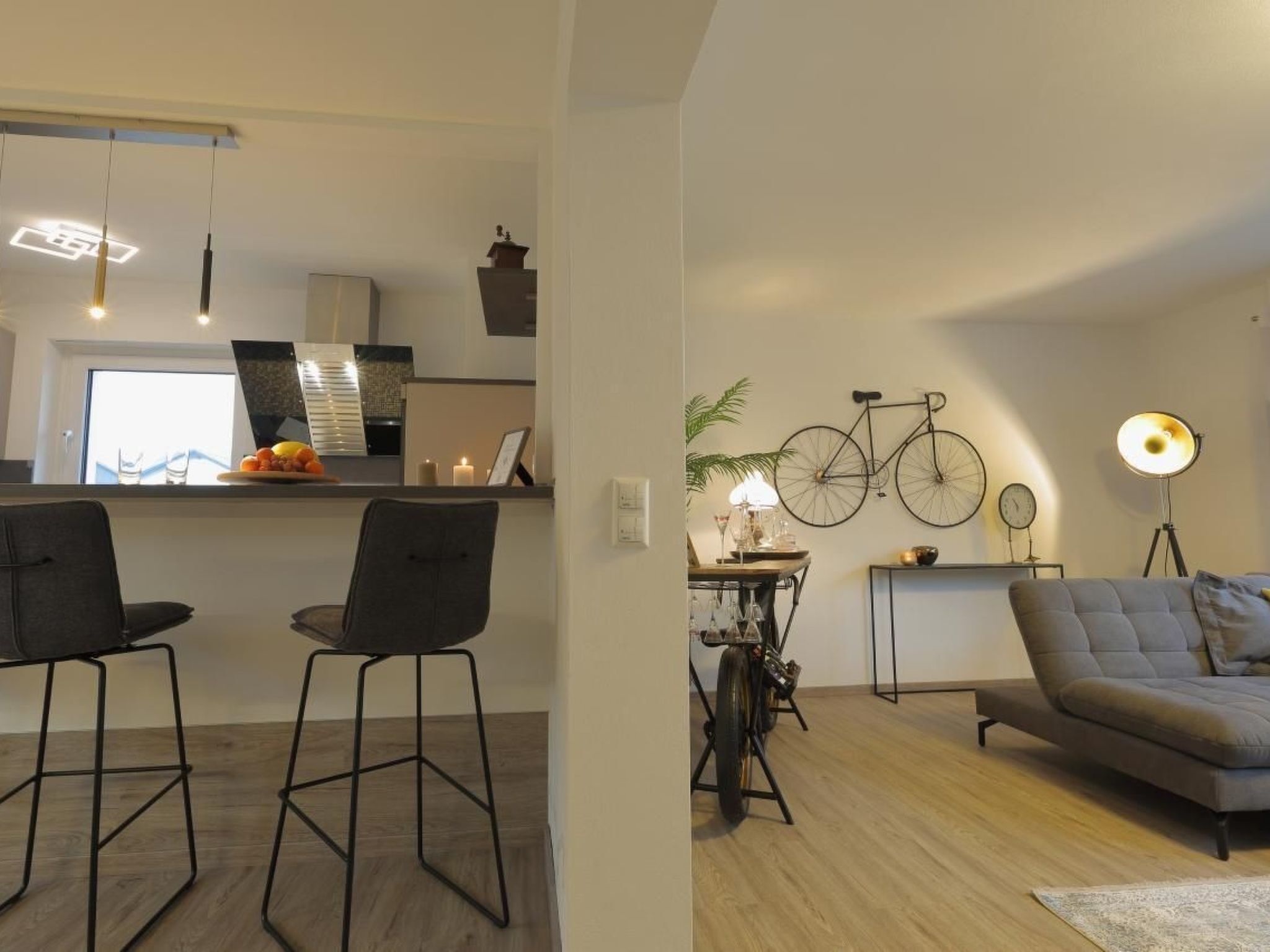 A modern living room with a sofa and chairs, a dining area with a table and chairs, and a kitchen in the background.