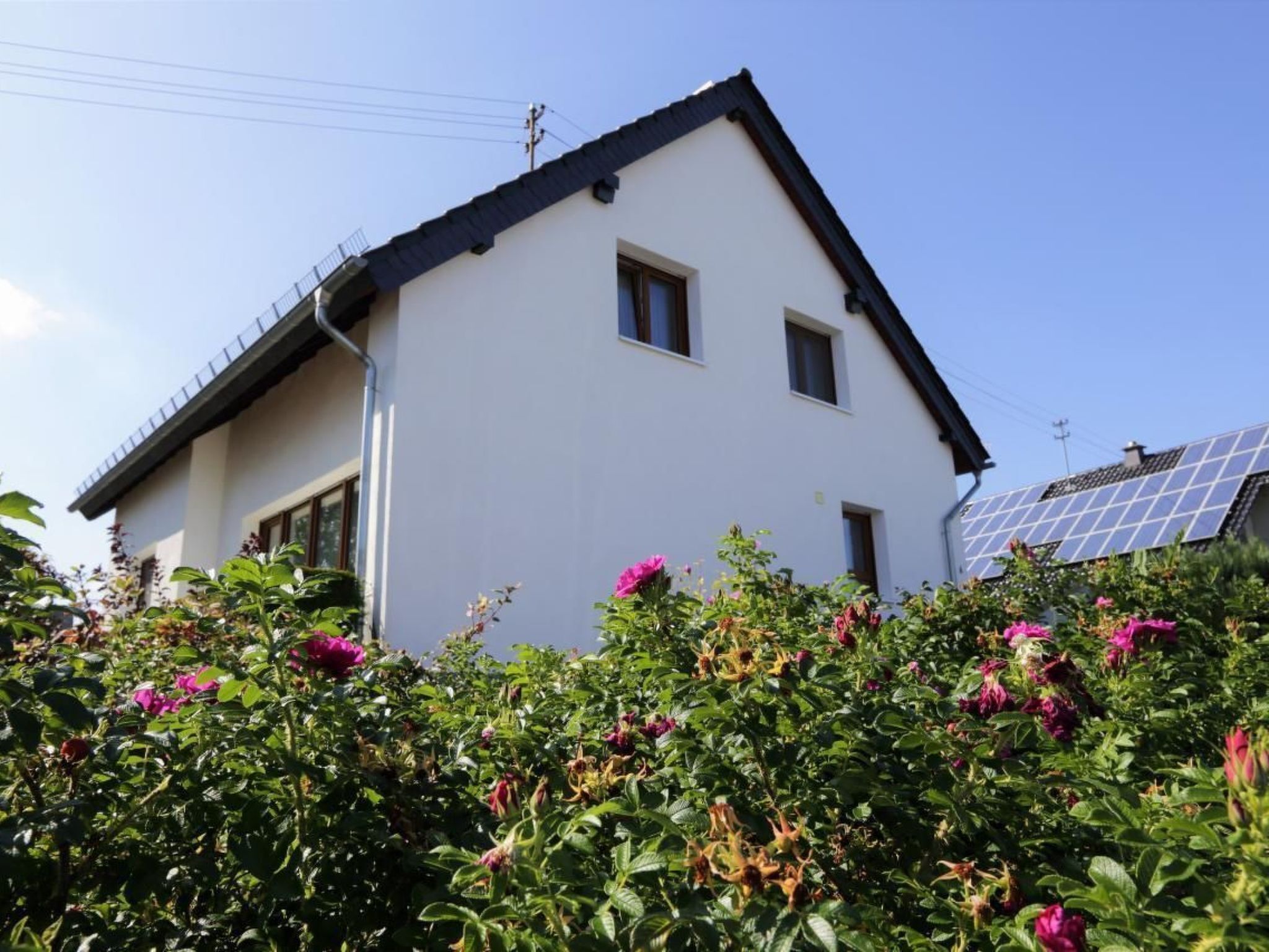 Une maison blanche à deux étages, avec un toit en pente et des panneaux solaires sur le toit.