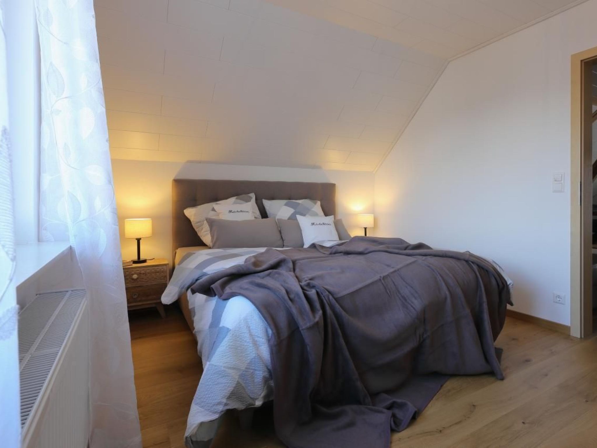 Quarto com cama, luminárias de cabeceira e janela com cortinas.