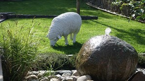 Een tuin met een wit schaap dat graast, omringd door rotsen en planten.