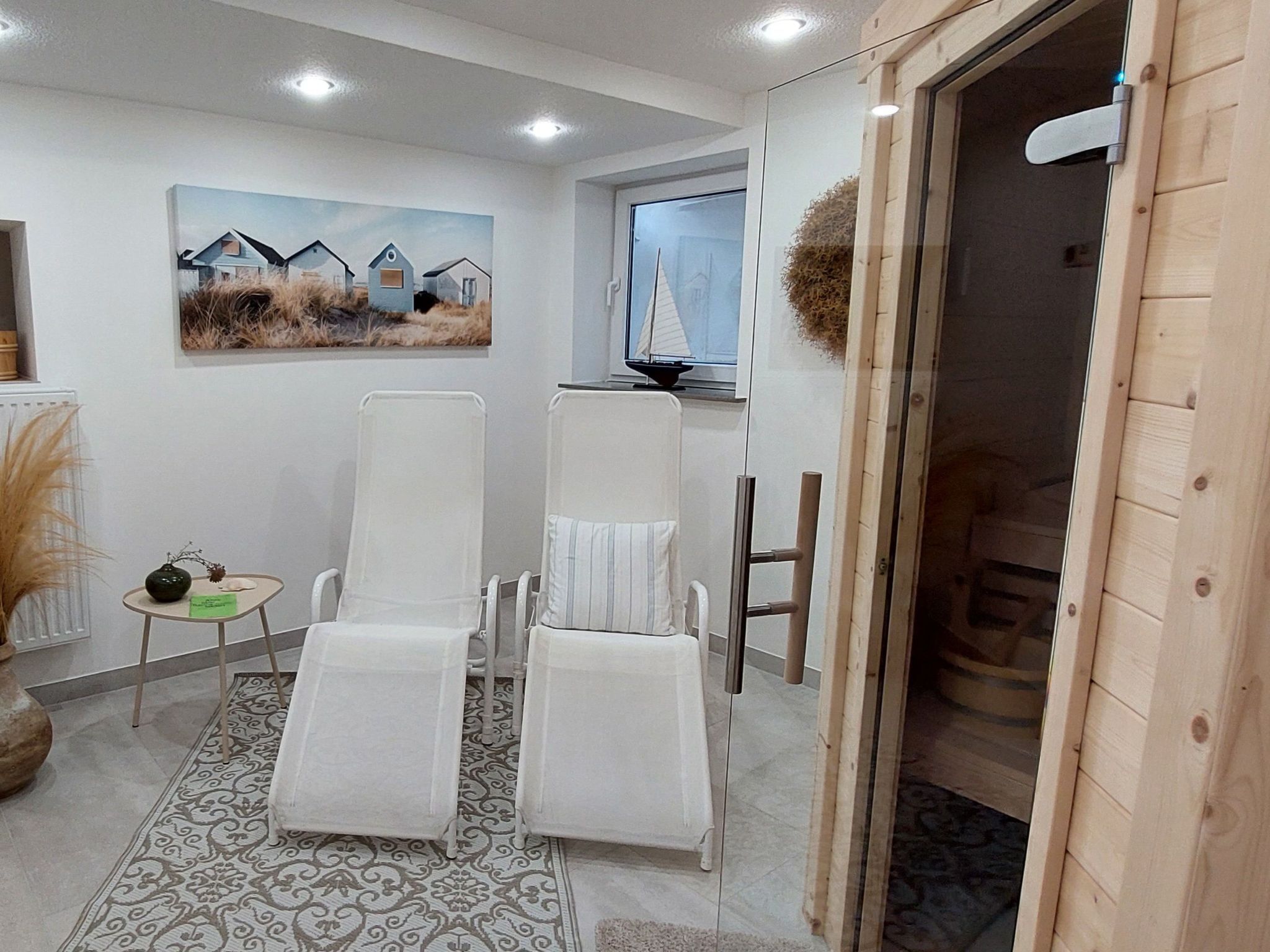 Ein Zimmer mit zwei weißen Lounge-Sesseln, einem gemusterten Teppich, einem Bild von Häusern und einer Holztür.