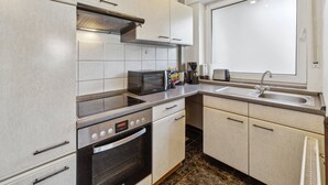 Eine moderne Küche mit weißen Schränken, einer Mikrowelle, einem Backofen, einer Kaffeemaschine und einem Fenster.