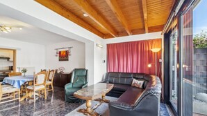 Ein geräumiger Wohnbereich mit Holzboden, einem Esstisch mit Stühlen, einer Couch und einer Glastür zum Außenbereich.