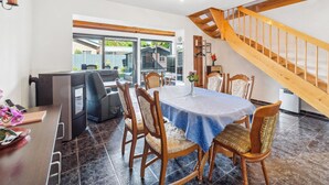 Ein Essbereich mit einem Tisch für vier Personen, umgeben von Holzsesseln. Eine Treppe mit Holzwandläufen führt auf eine erhöhte Ebene.