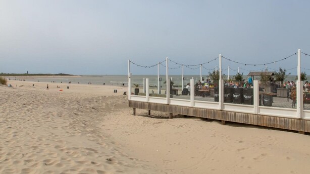 Een terras aan het strand met houten balustrade, lichtjes en buitenmeubels.