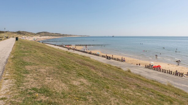 En strand vid kusten med en asfalterad gångväg, en sandstrand och fri utsikt över havet.