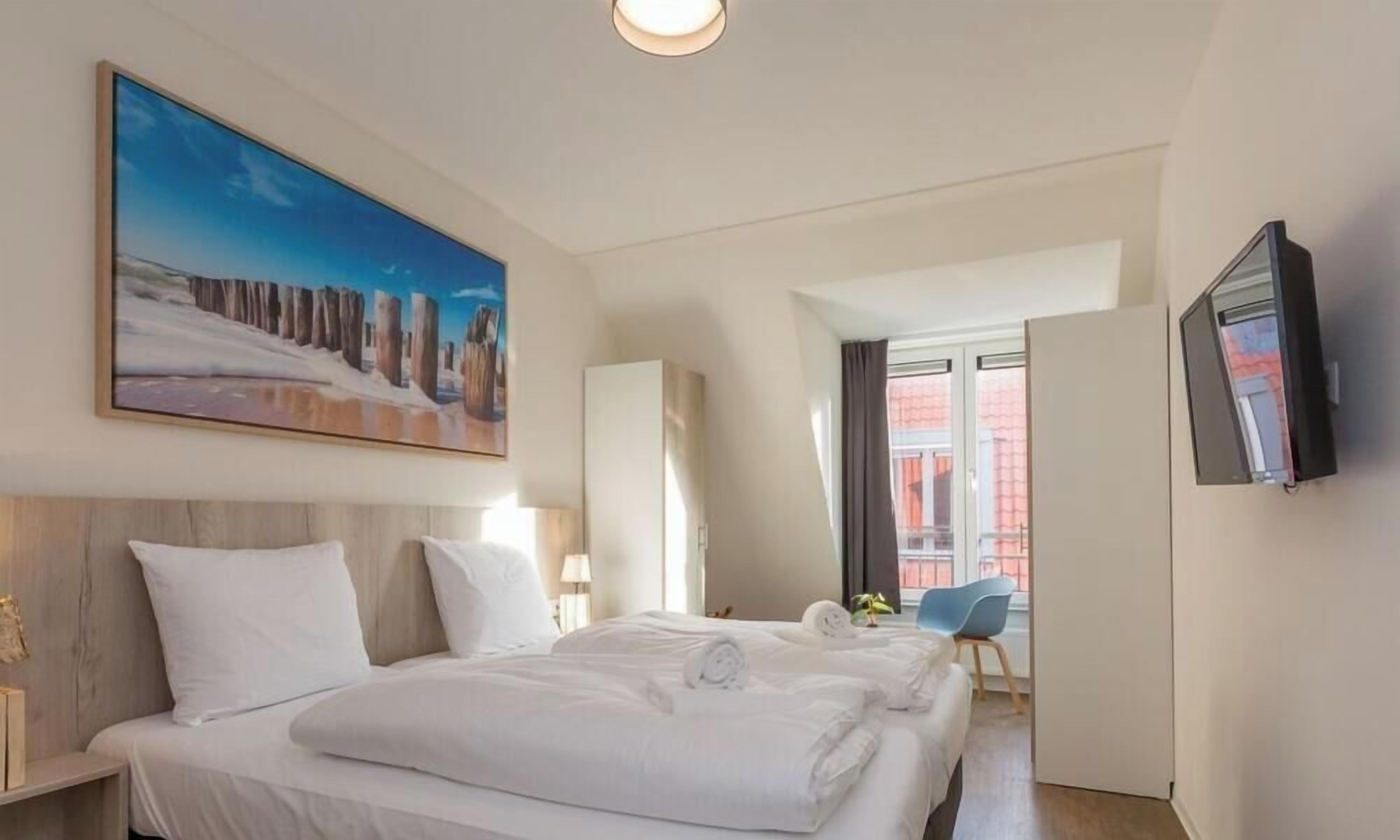 Ein Hotelzimmer mit zwei Betten, einem Gemälde, einem Fernseher und Blick auf ein Gebäude.