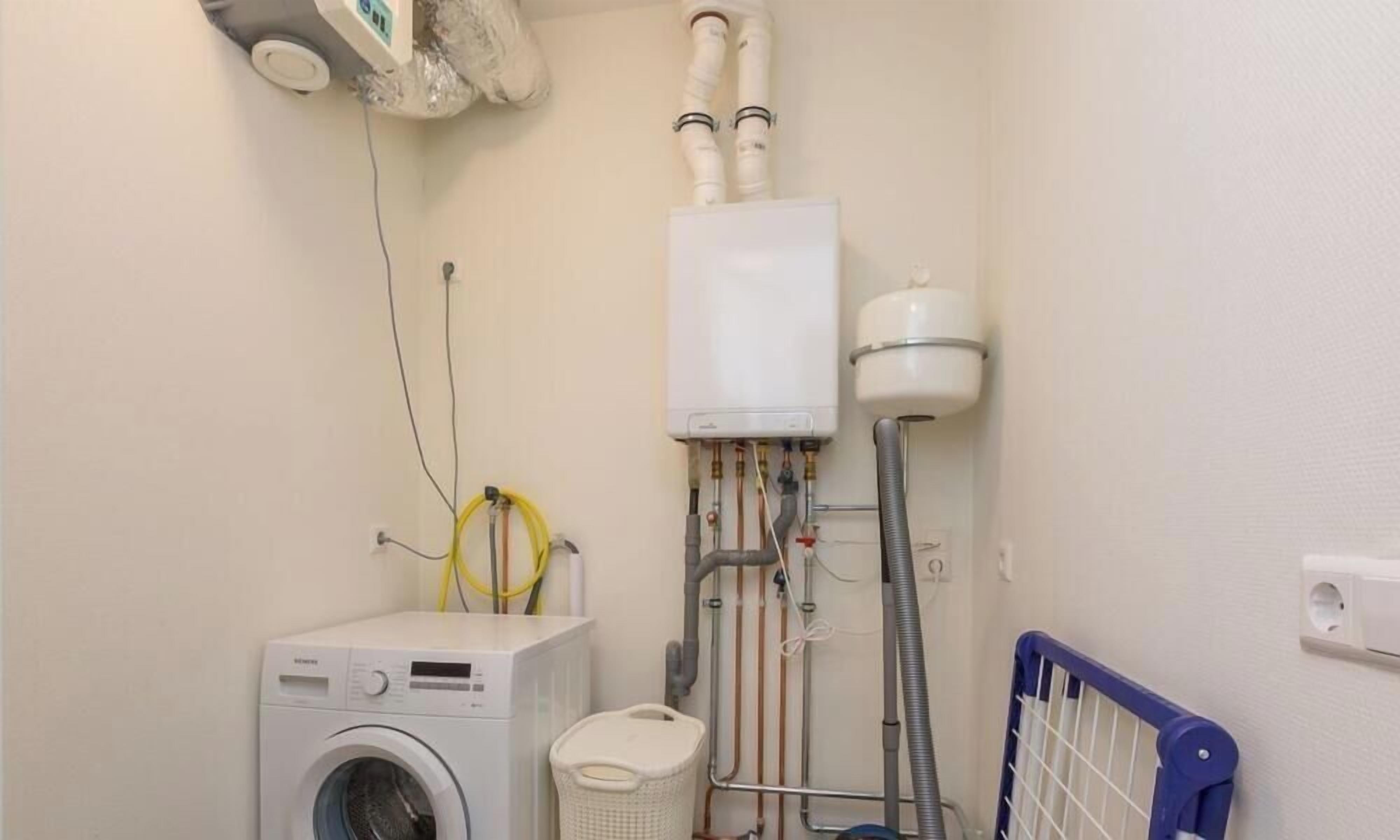 A laundry room with a washing machine, a water heater, and a radiator.