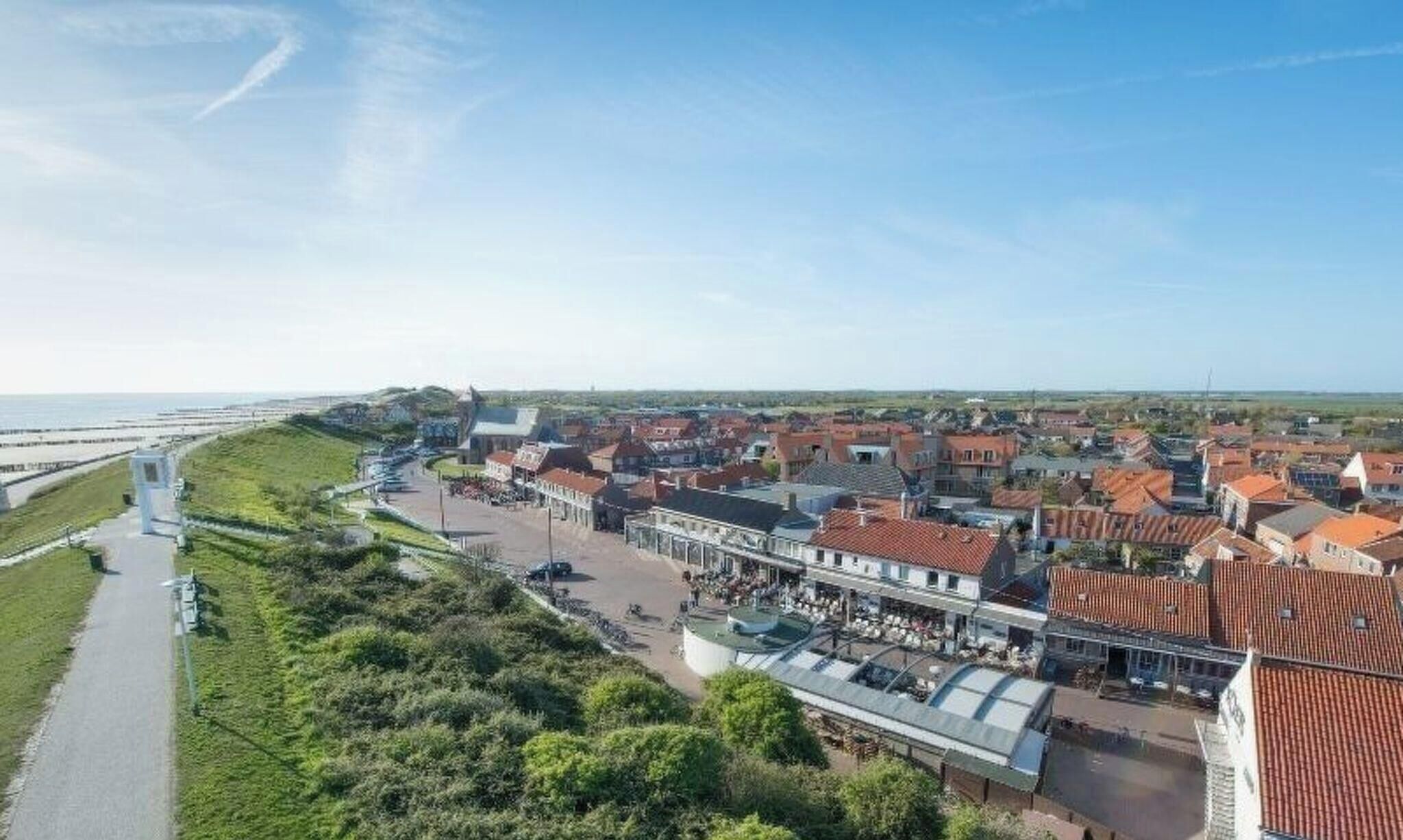 Un pueblo costero con una calle central flanqueada por edificios, un paseo marítimo y vistas al mar.