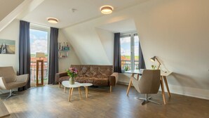 En moderne stue med en brun lædersofa, to hvide sofaborde og et spisebord. Der er tre loftslamper, store vinduer med gardiner, og udsigt til bygninger udefra.