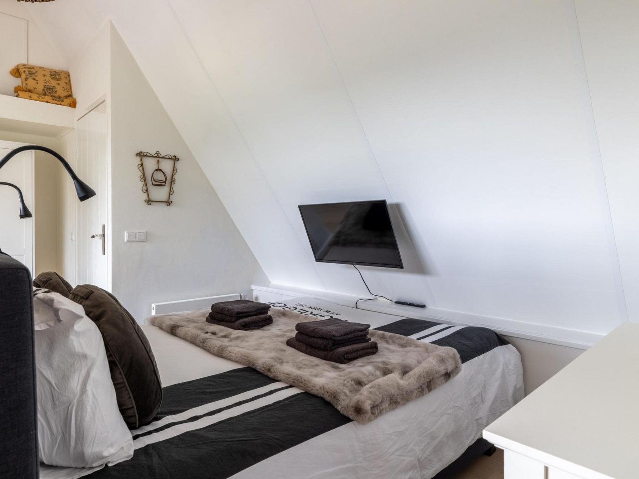 Une chambre avec un lit, un téléviseur fixé au mur et une fenêtre.
